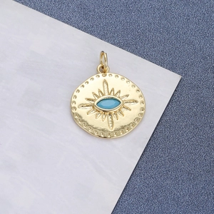 Close-up of a gold-plated medallion pendant with a turquoise stone and evil eye sunburst motif