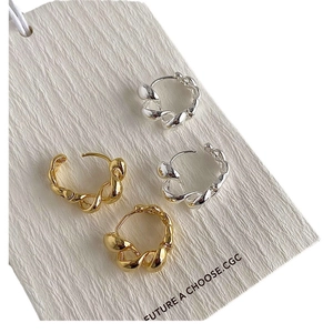 Polished twist rope hoop earrings in gold and silver finish on white textured card