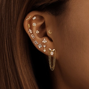 Close-up of gold helix piercings with chain fringe and geometric zircon studs on ear
