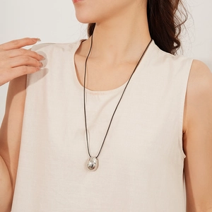 Détail d'un pendentif goutte en argent sur cordon noir porté avec un haut en lin beige