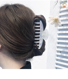 Close-up of a large iridescent blue hair claw clip worn by a model in a breezy summer setting