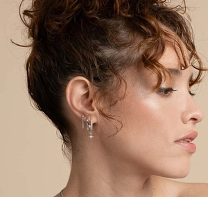 Macro detail of S925 silver star drop earrings and zircon hoop studs on female model