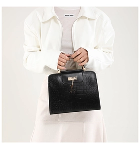Detail of black crocodile-embossed leather handbag with gold handle and deer pendant