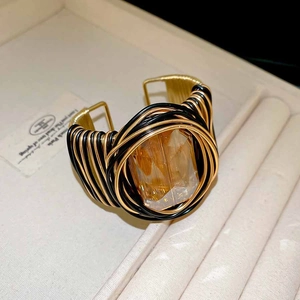 Gros plan d'un grand cristal ambré sur bracelet manchette tressé bicolore noir et doré chic