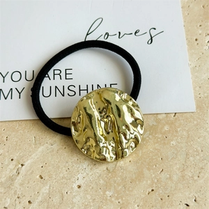 Close-up of black elastic hair tie with irregular textured gold metal piece on stone background