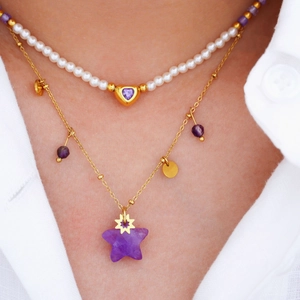 Layered gold necklaces with purple heart and star pendants on white pearl chain