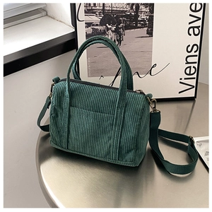 Close-up of a green corduroy Boston bag with top handles on a vintage metal table