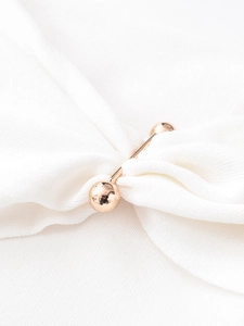 Detail of rose gold metal decorative fastener on white ribbed knit fabric top