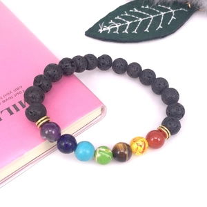 Detalle de una pulsera energética de chakra en piedra de lava negra sobre un libro rosa