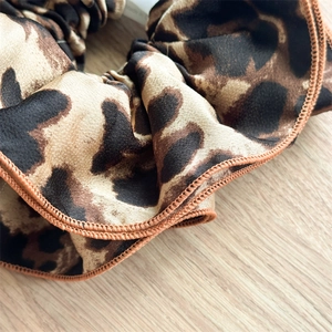 Close-up of leopard print satin hair scrunchie with detailed stitching on wooden surface