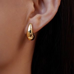 Close-up of elegant gold droplet C-shaped double earrings worn on female model's ear