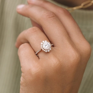 Elegant rose gold halo engagement ring featuring a central round stone and paved band