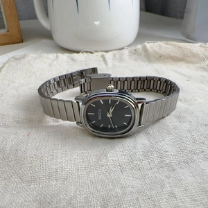 Detailed macro view of black oval dial with silver markers and metal link strap