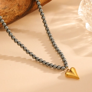 Elegant gold heart pendant necklace with dark grey pearls displayed on a minimalist background