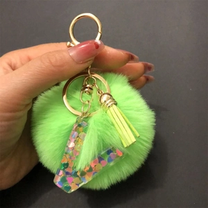 Detail of neon green pompom keychain with gold chain and heart sequin resin pendant