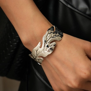 Detail of silver leaf shaped open cuff bracelet with polished metallic texture and engraving