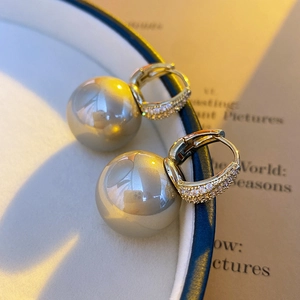 Detailed macro view of a gold-toned zircon hoop earring with a lustrous grey pearl drop