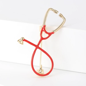 Macro detail of gold stethoscope brooch with red enamel on professional white background