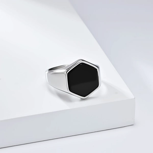 Detail of a minimalist hexagonal signet ring with black inlay on a white geometric stand