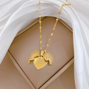 Macro view of gold heart necklace with sparkling rhinestone wings on luxury white silk