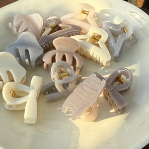 Close-up of assorted Morandi color claw clips and hair accessories in a white ceramic bowl