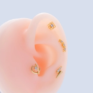Detailed view of gold studs with flower, star and lightning shapes on a silicone ear model