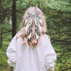 Silver metallic bow hair clip with long ribbons worn on model's pink hair in nature