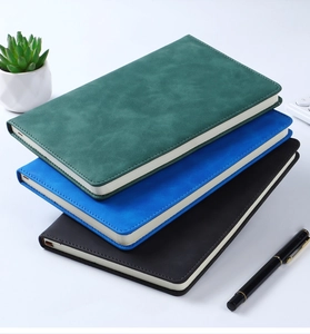 Close-up of three PU leather business notebooks in green, blue, and black with a pen