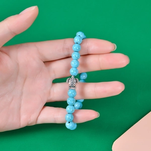 Close-up of blue 8mm stone bead bracelet with silver turtle charm on a person's wrist