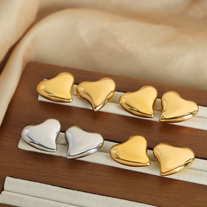 Polished heart-shaped stud earrings in gold and silver finish on a wooden display stand