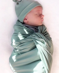 Close-up of soft sage green swaddle blanket and newborn beanie on white faux fur background