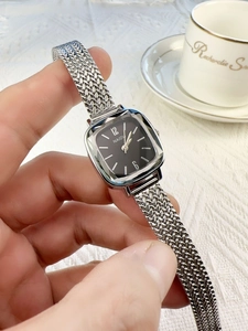 Elegant women's square silver mesh watch with black dial held in a lifestyle setting
