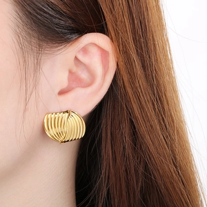 Detailed close-up of golden wavy quilted heart stud earrings on a model's ear