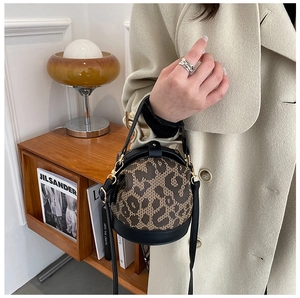 Close-up of leopard print and black PU leather bucket bag held by a model in a cozy setting