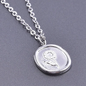 Macro shot of silver oval stainless steel pendant with sunflower engraving detail