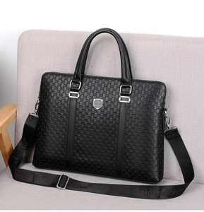 Macro shot of black textured leather laptop bag showing logo plaque and detachable strap