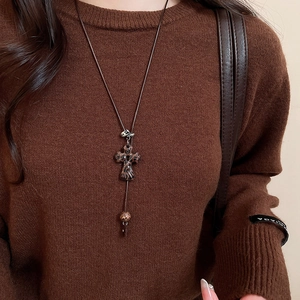 Détail du pendentif croix motif léopard avec perle tête de mort sur un pull marron