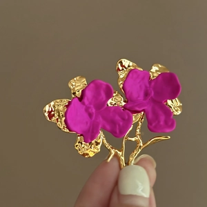 Detail of orchid earrings with magenta matte petals and golden textured metal stems