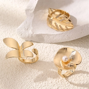 Golden rings set with monstera leaf, butterfly and pearl flower on a stone surface