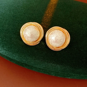 Detail of round gold plated earrings with white cotton pearls on green velvet