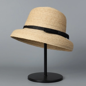 Close-up of raffia sun hat with black mesh ribbon and bow on minimalist stand