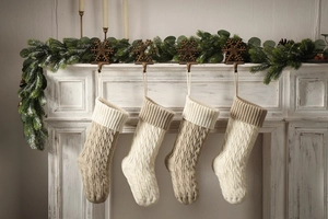 Cozy knit Christmas stockings in beige and white hanging on fireplace with pine decor