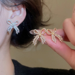 Close-up of sparkling bow earrings with inlaid zircons shown on a model ear and hand