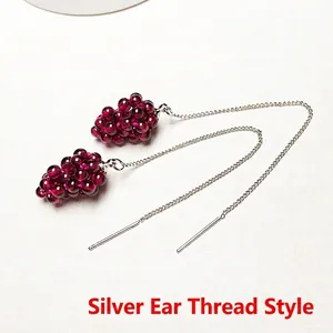 Detail of handmade grape-shaped garnet earrings with silver ear threads and red beads