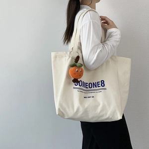 Detail of a large cream canvas tote bag with blue lettering and orange plush charm