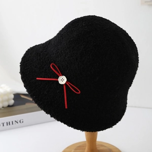 Plush black lamb wool bucket hat with a red bow and floral button on a wooden stand