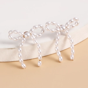 Close-up of handmade woven pearl bow earrings with elegant fringe detail on white stone