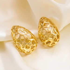 Macro shot of gold hollow teardrop earrings resting on elegant cream silk fabric