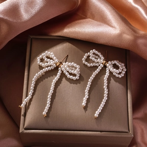 Detailed view of elegant bow-shaped earrings made of woven pearls and gold tassels
