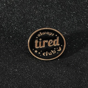 Close-up of Always Tired Club enamel pin with gold lettering on a glitter background